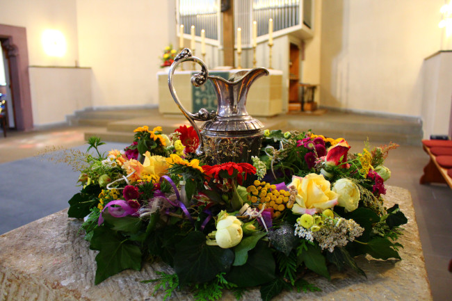 Taufstein mit Blumenkranz und Taufkanne